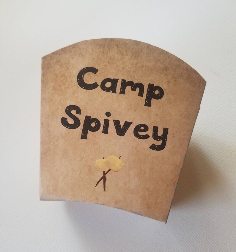 May include: A brown paper cup with the text "Camp Spivey" printed in black. There are two yellow marshmallow drawings on sticks.
