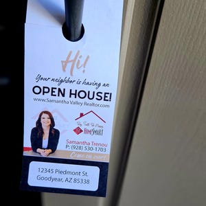 May include: A white door hanger with a photo of a woman and text that reads "Hi! Your neighbor is having an OPEN HOUSE! www.SamanthaValleyRealtor.com Buy Sell Be Happy HOMESMART Samantha Trenou P: (928) 530-1703 Come on over! 12345 Piedmont St. Goodyear, AZ 85338"
