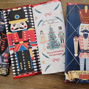 May include: Three chocolate bar wrappers featuring a nutcracker theme. The wrappers are decorated with a black and white checkered pattern, a watercolor illustration of a Christmas tree, and a blue and gold pattern. The text on the wrappers reads "Let's go nuts!" "Welcome to The Nathouse" and "Let's get this party CRACKIN".