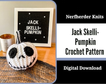 May include: A white crocheted Jack Skellington pumpkin with black eyes and a stitched mouth. The pumpkin is sitting on a black and white crocheted surface. A sign behind the pumpkin reads "Jack Skelli-Pumpkin".