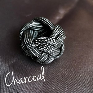 May include: A charcoal gray paracord knot, also known as a monkey fist, is a decorative knot that can be used as a keychain or a paperweight.