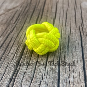May include: A bright yellow paracord knot, also known as a cobra knot, is tied in a circular shape. The knot is made with a thick, neon yellow cord and is sitting on a weathered wooden surface.