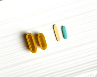 May include: A pair of mustard yellow oval-shaped earrings with a hollow center. The earrings are on a white surface.