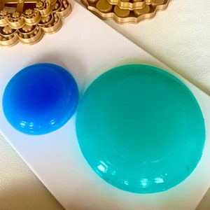 May include: Three gold-colored metal cookie cutters shaped like flowers, a blue and a turquoise round silicone mold.