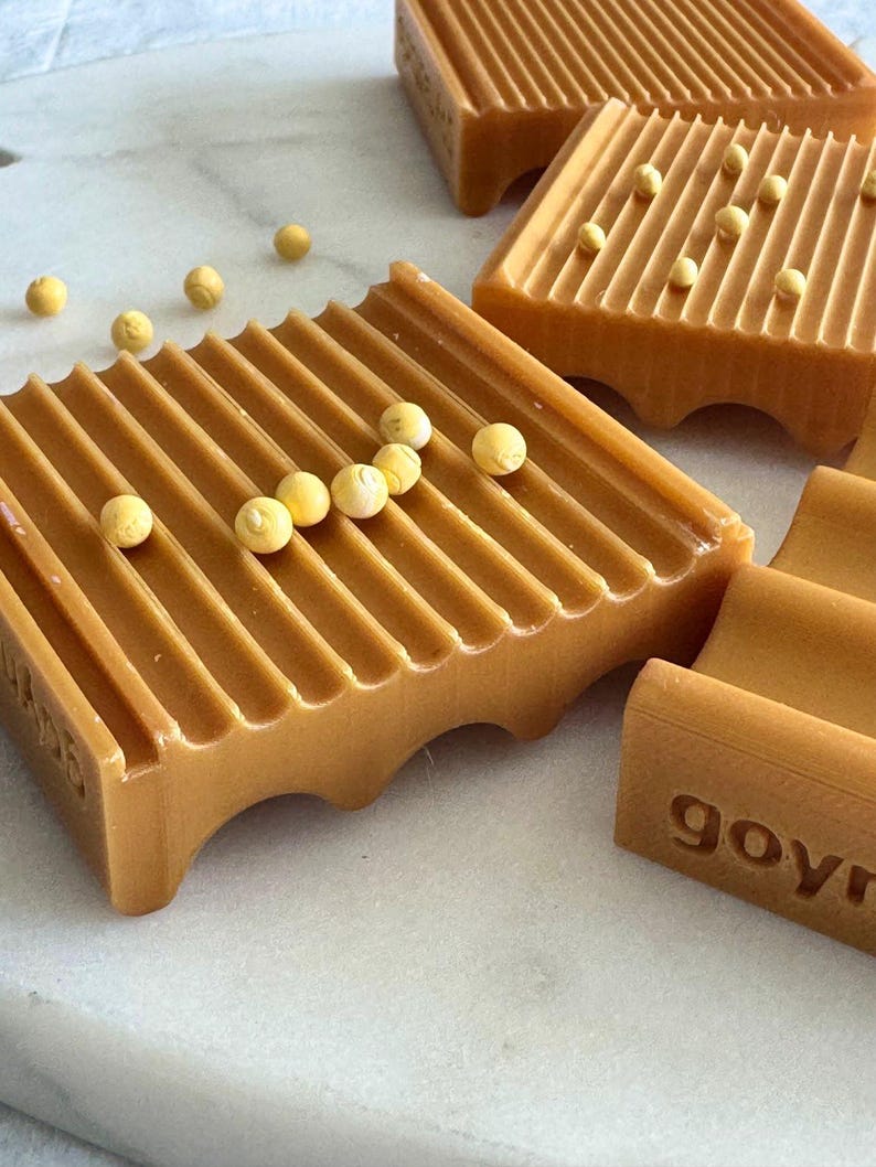 May include: Close-up of several brown soap dishes with a grooved design. Small yellow spheres are scattered on and around the soap dishes. The word "govr" is visible on the side of one dish.