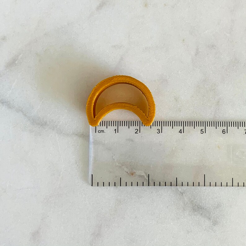 May include: A yellow plastic crescent moon cookie cutter measuring approximately 2 cm in diameter.