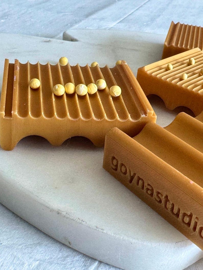 May include: Close-up of several amber-colored soap dishes with a grooved design. Each dish has a series of parallel ridges and is adorned with small, round, yellow beads. The text "goynastudio" is visible on one dish.