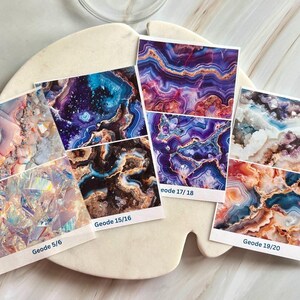 Peut inclure: Plusieurs cartes imprimées présentant des motifs abstraits de géodes aux couleurs vives : bleu, violet, marron et blanc. Chaque carte est étiquetée avec "Geode" et un numéro. Les cartes sont disposées sur un plateau blanc de forme organique.