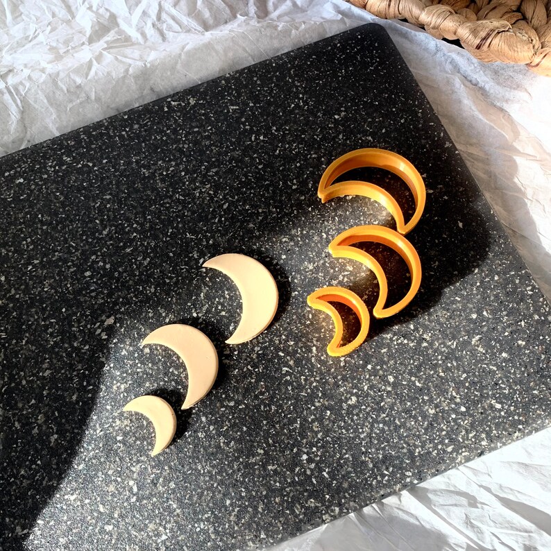 May include: A set of five cookie cutters in the shape of crescent moons. The cutters are made of yellow plastic and are arranged in a row on a black surface.