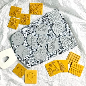 May include: A set of 16 rubber stamps featuring various designs, including geometric shapes, floral patterns, and abstract art. The stamps are arranged on a white surface with black polka dots.