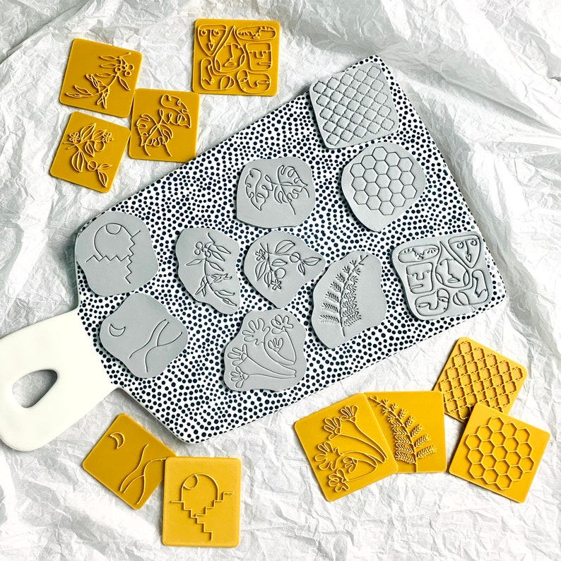May include: A set of 16 rubber stamps featuring various designs, including geometric shapes, floral patterns, and abstract art. The stamps are arranged on a white surface with black polka dots.