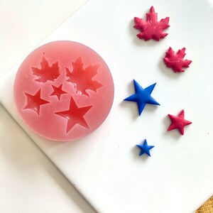May include: A pink silicone mold with four leaf shapes and three star shapes. There are five separate red and blue shapes on a white surface.