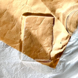 May include: A clear plastic ruler with a rounded edge and a measurement scale on the right side. The ruler is on a brown paper surface with the text "goynastudio" printed on the bottom.