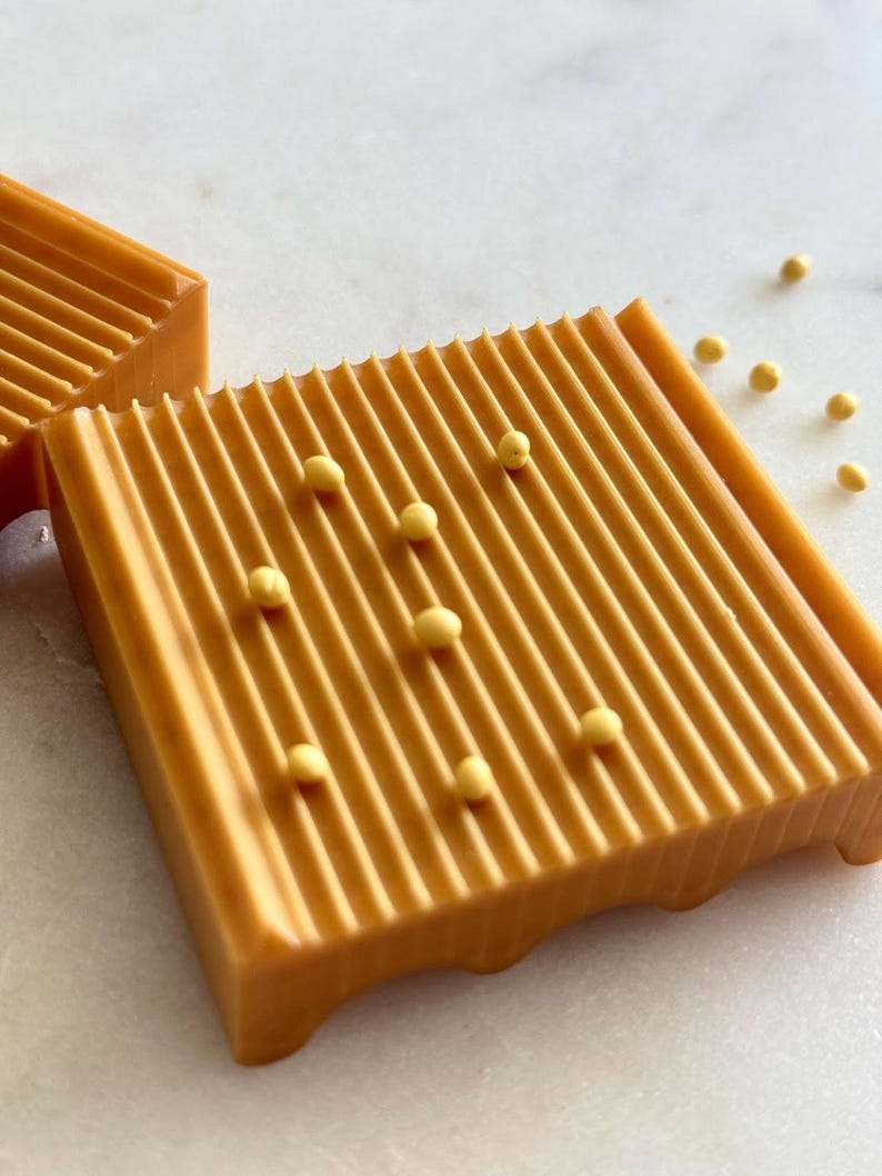 May include: Close-up of two rectangular, orange-colored bars with parallel ridges. Small, yellow spherical objects are scattered around the bars. The bars have a smooth, glossy finish and are set against a white background.