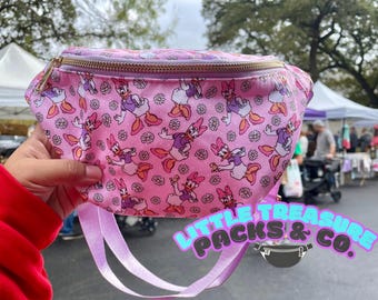 Op de afbeelding: Een roze heuptas met een all-over print van Daisy Duck-figuren en witte madeliefjes. De tas heeft een goudkleurige metalen ritssluiting aan de bovenkant en een lichtpaarse verstelbare riem. De stof is voorzien van het herhalende patroon.