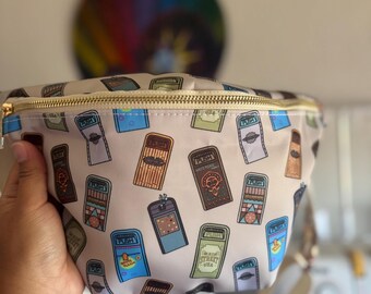 May include: A beige bum bag featuring an all-over print of various colourful trash cans, each with a PUSH label. The bag has a gold-toned zip closure along the top and an adjustable cream-coloured strap attached to the sides.