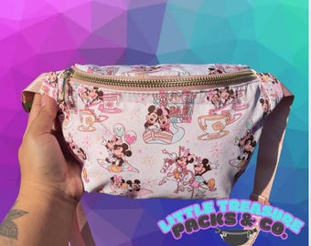 May include: A pink and white fanny pack with a gold zipper and a print of Mickey Mouse and Minnie Mouse characters. The pack has a pink strap and the text "Little Treasure Packs & Co." is printed on the strap.