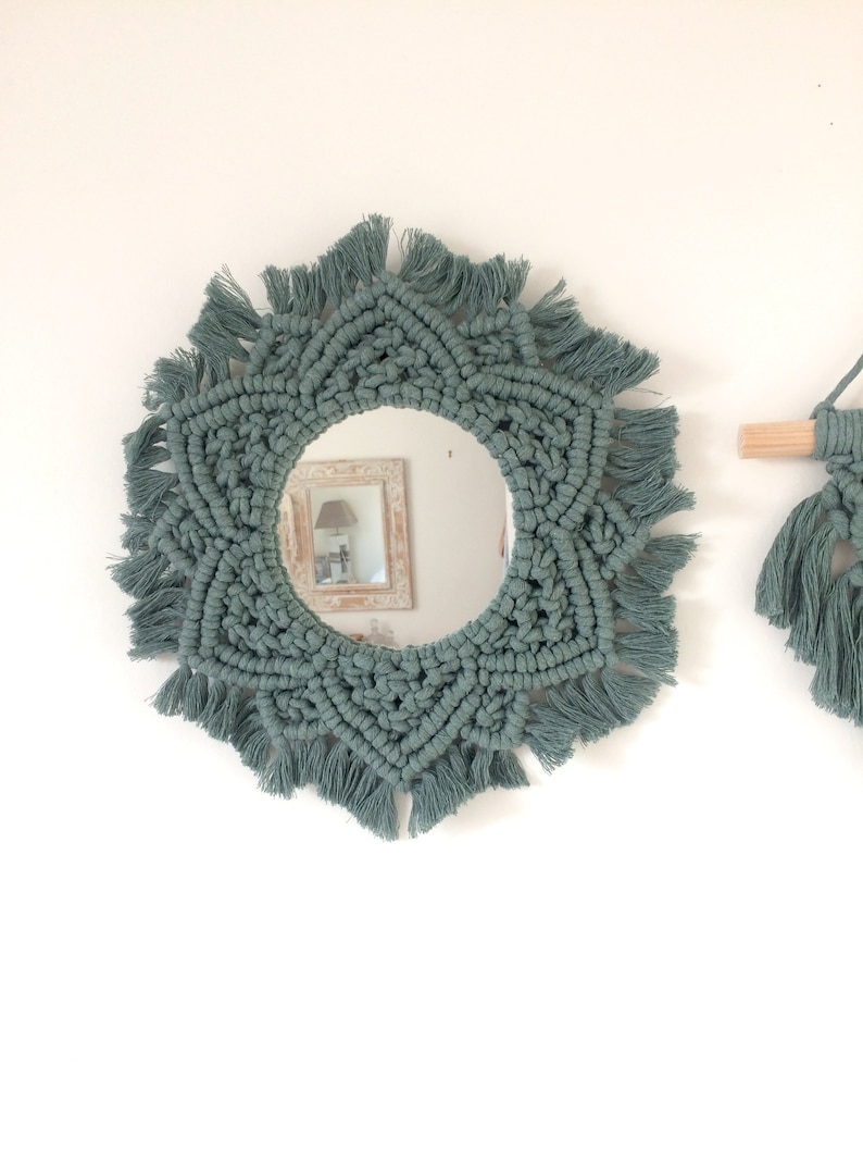 Peut inclure: Un miroir rond avec un cadre en macram&eacute; de couleur vert sauge. Le cadre a un motif en &eacute;toile avec des franges autour des bords.