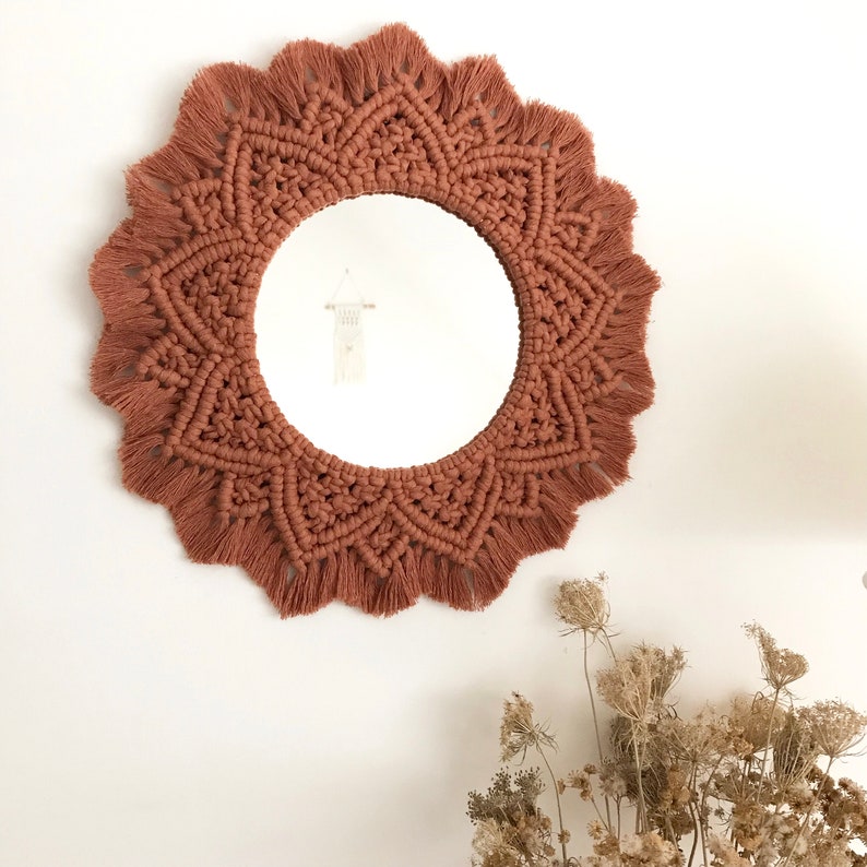 Peut inclure: Un miroir rond en macram&eacute; avec une frange brune. Le miroir est accroch&eacute; &agrave; un mur blanc.