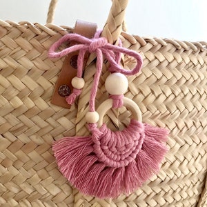 Peut inclure: Un porte-clés en tissu tissé rose et marron avec des perles en bois pend à un sac en paille tissé.