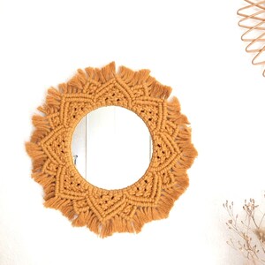 Peut inclure: Un miroir rond avec un cadre en macram&eacute; de couleur jaune moutarde. Le cadre est fait de fil &eacute;pais avec une frange autour du bord.