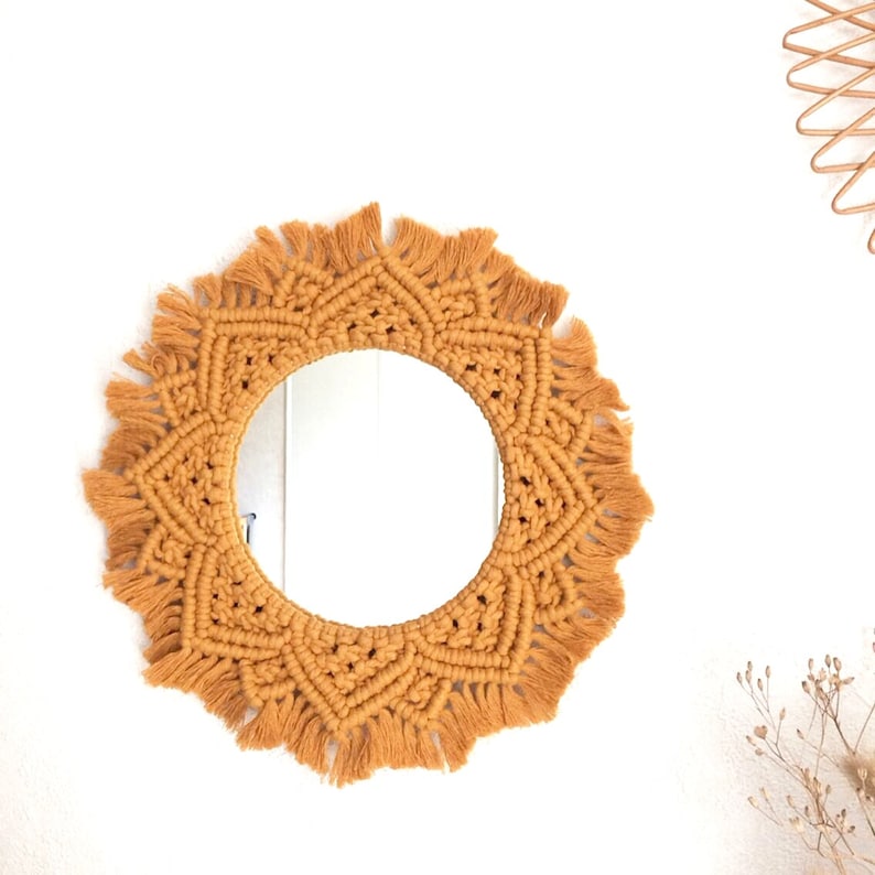 Peut inclure: Un miroir rond avec un cadre en macram&eacute; de couleur jaune moutarde. Le cadre est fait de fil &eacute;pais avec une frange autour du bord.