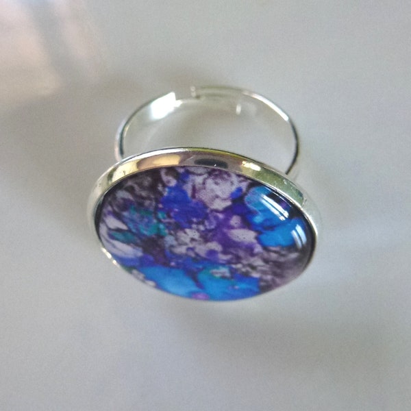 bague ajustable composée d'un cabochon rond bleu/violet/blanc monté sur un support en métal argenté