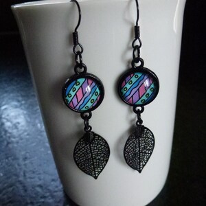 Randiga cabochonörhängen (gul/grön/blå/rosa/lila), berlocker i svart metallblad, monterade på svarta metallstolpar och krokar