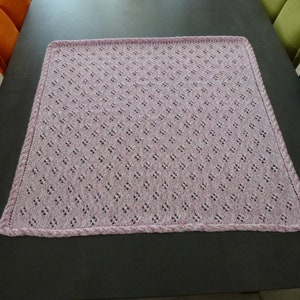 Può includere: Una coperta lavorata a maglia lilla chiaro con un motivo a rombi e un bordo intrecciato. La coperta è quadrata e sembra fatta a mano. Il colore è una tonalità tenue e delicata di viola.
