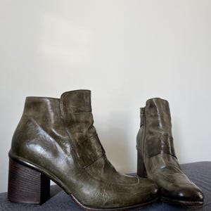 May include: A pair of dark green leather ankle boots with chunky heels. The boots have a buckle detail on the side and a zipper on the back.