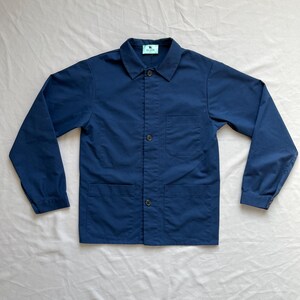 May include: A navy blue workwear jacket with a button-up front, two chest pockets, and a single pocket on the left sleeve. The jacket has a small label on the left side of the chest that reads "Glover".