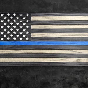 May include: A wooden American flag with a blue stripe across the middle, representing the thin blue line. The flag is made of different shades of wood, creating a unique and rustic look.