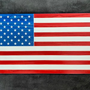 May include: A wooden American flag with red and white stripes and blue stars. The flag is painted on a wood grain surface.