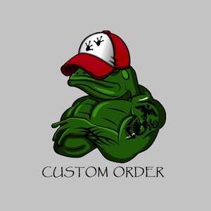May include: A green frog wearing a red baseball cap with white paw prints and a tattoo of the Marine Corps emblem on its arm. The frog has a muscular build and is looking to the side. The text "CUSTOM ORDER" is below the frog.