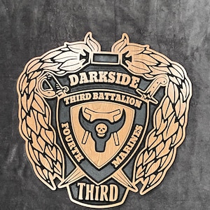 May include: A wooden plaque with a black and brown design. The plaque features a skull and crossbones, a bull's head, and the words "DARKSIDE THIRD BATTALION FOURTH MARINES THIRD".