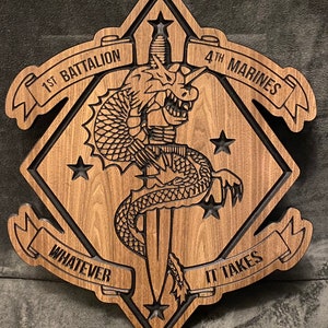 May include: A wooden plaque with a black outline in the shape of a diamond. The plaque features a dragon wrapped around a dagger, with the words "1st Battalion 4th Marines" and "Whatever It Takes" on banners.