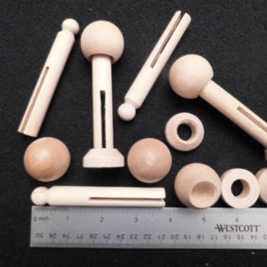 May include: A collection of unfinished wooden craft pieces, including dowels, spheres, and slotted components. A ruler with inch measurements is placed next to the wooden pieces. The items are arranged on a dark surface.