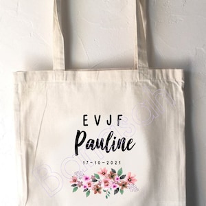 Könnte beinhalten: Eine weiße Canvas-Tragetasche mit schwarzem Text, der "EVJF Pauline 17-10-2021" lautet, und einem Blumendesign mit rosa und grünen Blumen.
