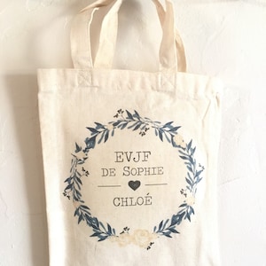 Puede incluir: Una bolsa de lona blanca con un diseño de corona floral azul. La corona tiene el texto "EVJF DE SOPHIE" y un corazón con el nombre "CHLOE" dentro.