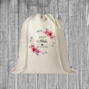 Może przedstawiać: Biała torba ze sznurkiem do ściągania z wzorem kwiatowego wianka. Wianek zdobią różowe i fioletowe kwiaty z zielonymi liśćmi. Wewnątrz wianka nadrukowany jest tekst "EVJF Malo 05-09-2020".