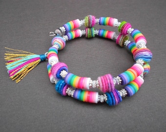 May include: A colorful bracelet made with rainbow striped beads, felt beads, and silver spacer beads. The bracelet has a turquoise, pink, and gold tassel.