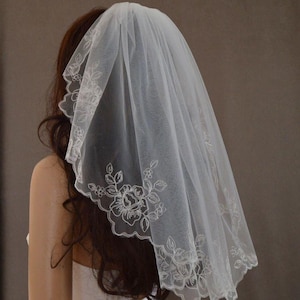 K&ouml;nnte beinhalten: Ein wei&szlig;er Brautschleier, 56 cm lang, mit einem gewellten Rand und floraler Stickerei. Der Schleier besteht aus einem transparenten Stoff und wird &uuml;ber dem Kopf getragen. Der Text "veil 22 inch" ist sichtbar.