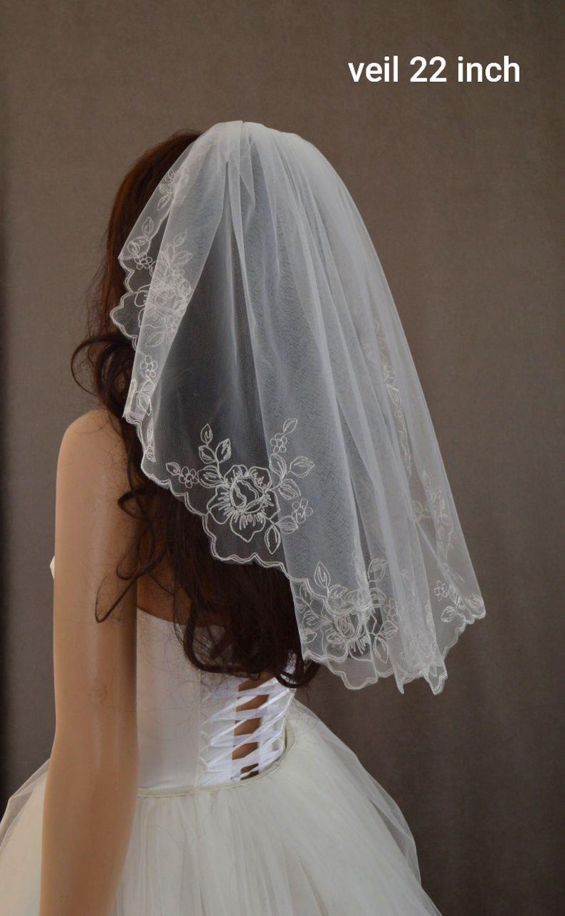 K&ouml;nnte beinhalten: Ein wei&szlig;er Brautschleier, 56 cm lang, mit einem gewellten Rand und floraler Stickerei. Der Schleier besteht aus einem transparenten Stoff und wird &uuml;ber dem Kopf getragen. Der Text "veil 22 inch" ist sichtbar.