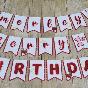 May include: A white and red banner with the text "Emerley's Berry 1st Birthday" decorated with strawberries and daisies.