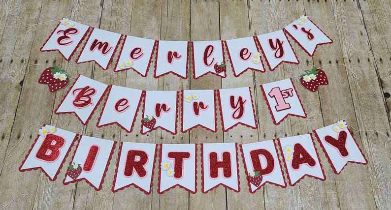 May include: A white and red banner with the text "Emerley's Berry 1st Birthday" decorated with strawberries and daisies.