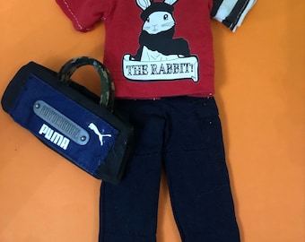 May include: Red and white striped t-shirt with a black and white rabbit graphic and the text "THE RABBIT!"  Black pants and a blue and black bag with the text "POWERHOUSE PUMA".