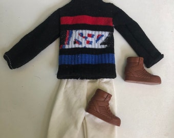 May include: A black sweater with a red, white, and blue striped pattern and a white graphic design. White pants and brown high-top shoes.