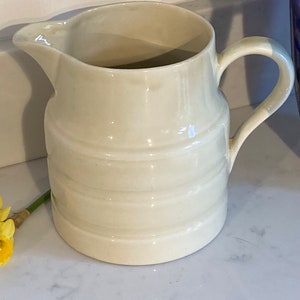May include: A white ceramic pitcher with a ribbed design. The pitcher has a rounded body and a handle.