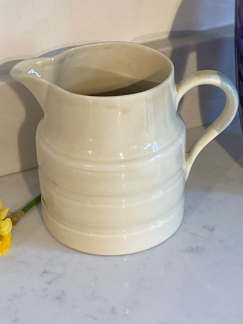 May include: A white ceramic pitcher with a ribbed design. The pitcher has a rounded body and a handle.