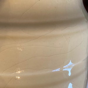 May include: A close-up of a white ceramic pitcher with a textured surface. The pitcher has a slightly rounded shape and a smooth, glossy finish.